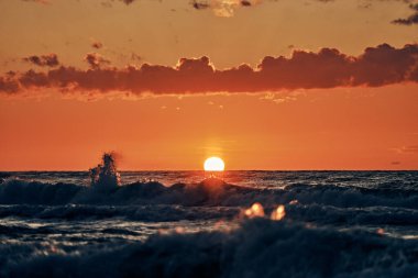 Mavi deniz dalgaları üzerinde yarım güneş, denizin üzerinde güzel gün batımı. Turkuaz deniz dalgaları dramatik güneş ışığı altında, gün batımında turuncu güneşten, atmosferik deniz dalgalarıyla nefes kesici deniz manzarası.