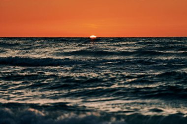 Mavi deniz dalgaları üzerinde yarım güneş, denizin üzerinde güzel gün batımı. Turkuaz deniz dalgaları dramatik güneş ışığı altında, gün batımında turuncu güneşten, atmosferik deniz dalgalarıyla nefes kesici deniz manzarası.