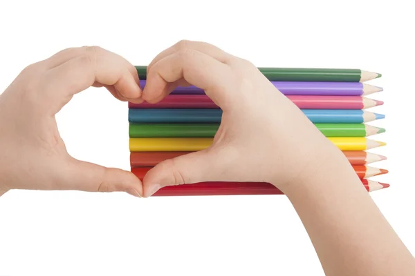 Les mains de l'enfant forment un cœur au-dessus des crayons de couleur — Photo