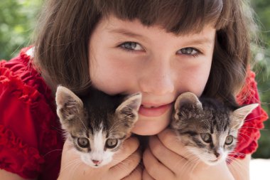 iki sevimli kedi yavrusu tutan küçük bir kız