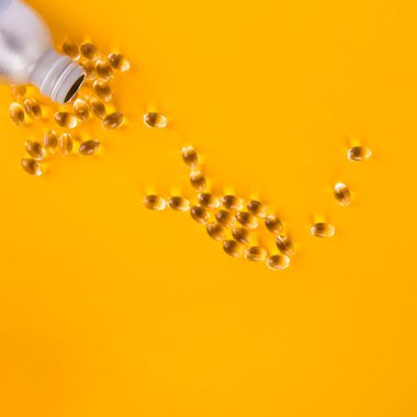 Omega 3 kapsülleri sarı bir zemin üzerinde balık şeklinde dizilmiştir.