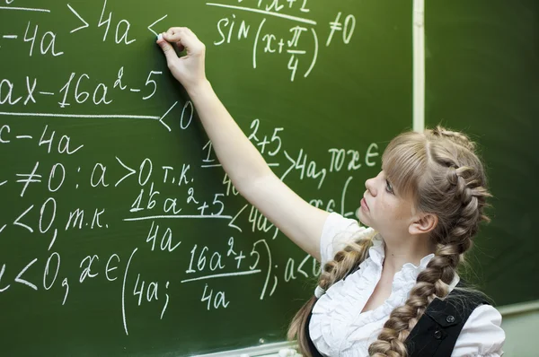 Schoolgirl at the blackboard writes — Stock Photo, Image