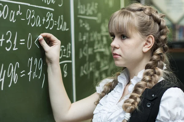 Schoolgirl at the blackboard writes — Stock Photo, Image