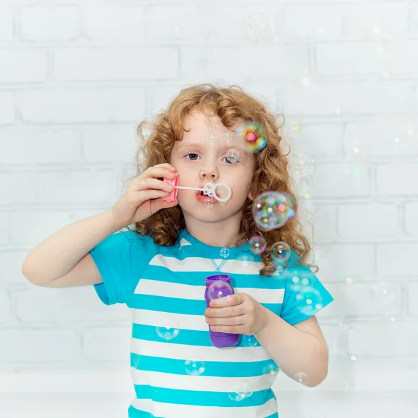 Curly girl blowing soap bubbles, on a light background in the st