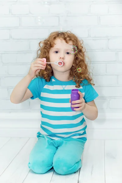 Curly girl blowing soap bubbles, on a light background in the st