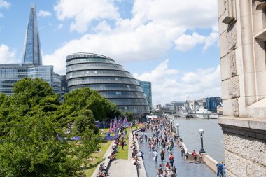 Londra, İngiltere. 11 Haziran 2022. Londra 'daki Tower Bridge yakınlarındaki Thames Nehri' nin güney kıyısındaki Queen 's Walk' ta yabancı turistler ve gezginlerle dolu gezinti güvertesi boyunca yürüyüş yapıyorlar.. 