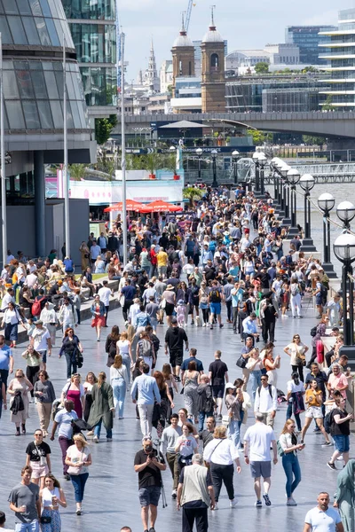 Londra, İngiltere. 11 Haziran 2022. Londra 'daki Tower Bridge yakınlarındaki Thames Nehri' nin güney kıyısındaki Queen 's Walk' ta yabancı turistler ve gezginlerle dolu gezinti güvertesi boyunca yürüyüş yapıyorlar.. 