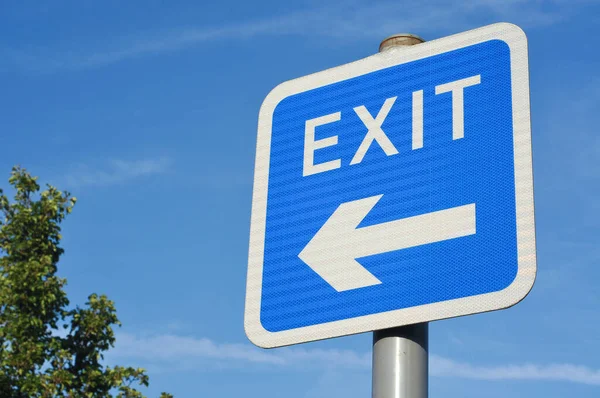 EXIT road sign with arrow symbol pointing to the left, against a clear blue sky.