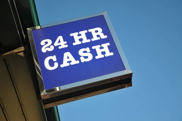 Low angle view of ATM - 24 HR CASH sign attached to building against a clear blue sky.