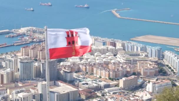 ジブラルタルだ 2022年9月5日 ジブラルタルの大都市圏を見下ろす高い視点 ジブラルタルの旗が前景に飛んでいます ドック 空港滑走路 タワーブロックを見ることができます — ストック動画
