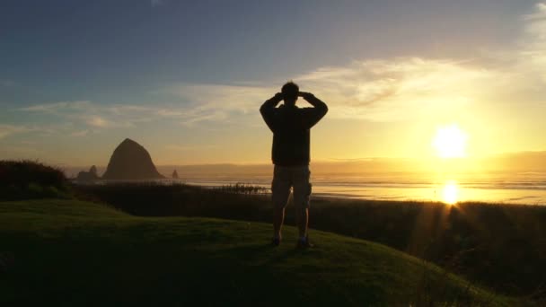 Man at Pacific Ocean near Cannon Beach looks out to sea as sun sets on beautiful day. — Stock Video