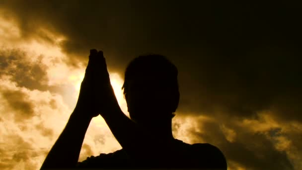 Personne silhouette sépare les mains priantes pour révéler le soleil qui brille à travers .