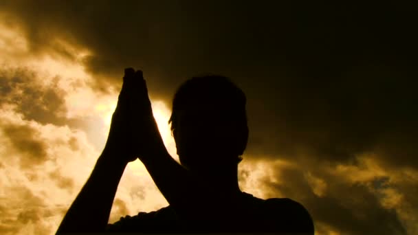 Person silhouetted separates praying hands to reveal sun shining through. — Stock Video