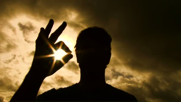 Persona silueta levanta la mano en el marco para dar una señal a-okay con el sol brillando a través de la lente de la cámara . — Vídeo de stock