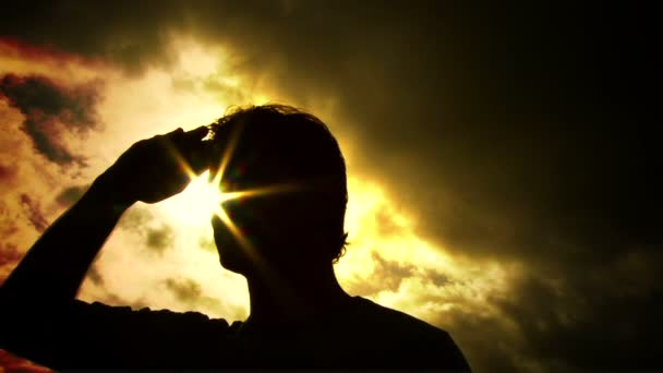 La persona silhouetted solleva il braccio e guarda fuori alla ricerca di qualcosa con il sole dietro . — Video Stock