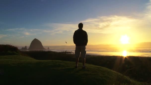 El hombre en el Océano Pacífico cerca de Cannon Beach mira hacia el mar mientras el sol se pone en un hermoso día . — Vídeos de Stock
