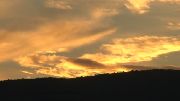 Coucher de soleil avec des nuages éclairés orange le temps passe sur la colline. Mouvement inverse pour un grand lever de soleil . — Video