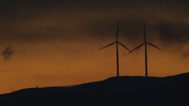 Două turbine eoliene care se rotesc de-a lungul dealului în Washington la apusul soarelui . — Videoclip de stoc