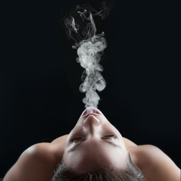 Woman blowing smoke against dark background. Studio fashion phot