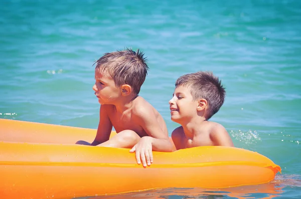 Dos hermanos jugando en la playa con colchón de aire . — Foto de Stock