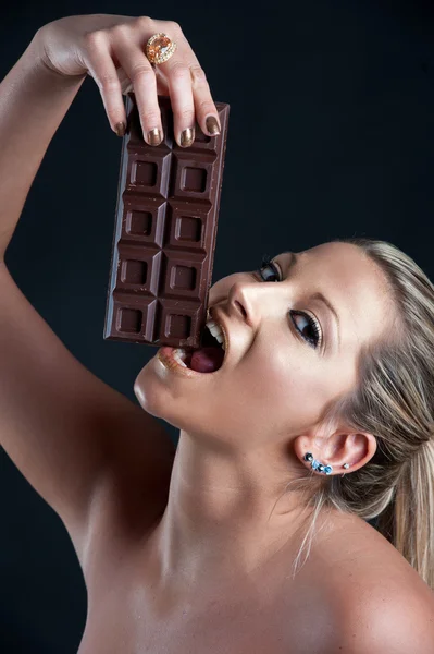 Beautiful woman with golden make up eating chocolate against black — Stock Photo, Image