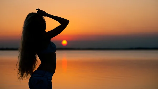 Gyönyörű fiatal nő sziluett naplementekor a strandon. — Stock Fotó