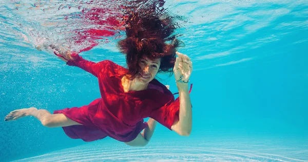 Подводная женщина с красным платьем в бассейне — стоковое фото
