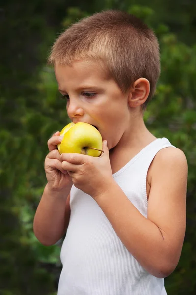 Porträtt av en liten pojke som äter ett äpple utomhus — Stockfoto