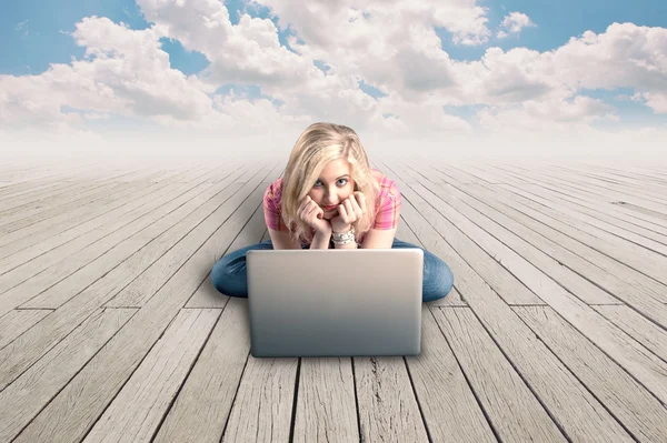 Hübsches Mädchen arbeitet an einem Laptop auf einem Holzboden und einem wolkenverhangenen blauen Himmel — Stockfoto