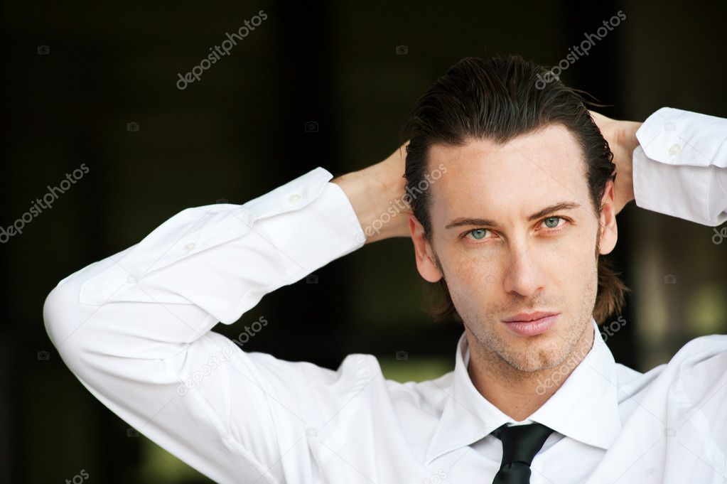 Confident young businessman looking at camera. Dark background