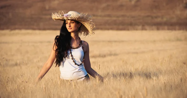 Jeune belle femme dans un champ de blé avec robe blanche et chapeau de paille — Photo