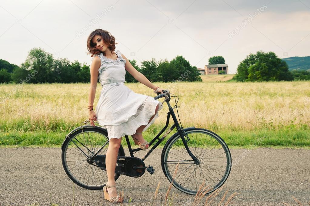 Pretty young woman relaxing with bike in a country road