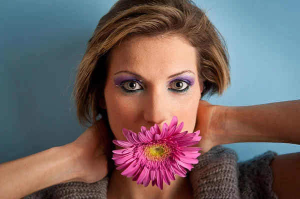 Portret van mooi meisje met gerbera bloem in haar mond tegen blauwe achtergrond — Stockfoto