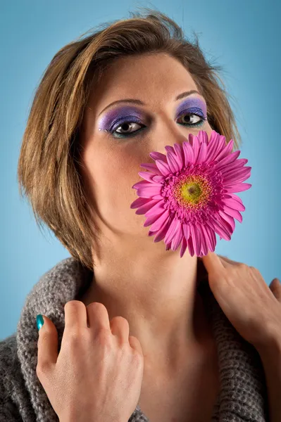 Portret van mooi meisje met gerbera bloem in haar mond tegen blauwe achtergrond — Stockfoto