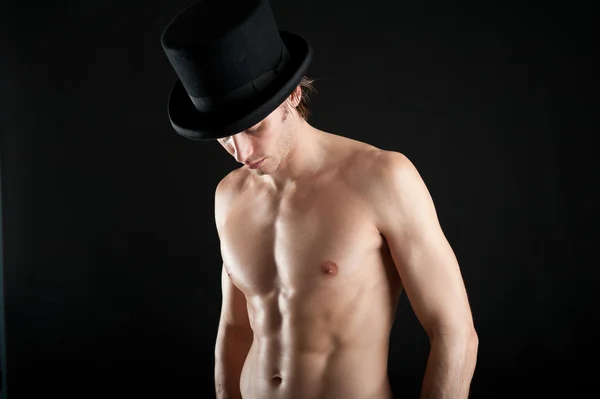 Молодой человек без рубашки с цилиндром на черном фоне — стоковое фото