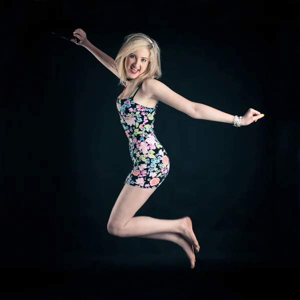 Attractive blond girl listening to music and jumping against black background — Stock Photo, Image