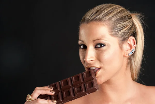 Hermosa mujer con maquillaje dorado comiendo chocolate sobre fondo negro — Foto de Stock