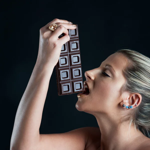 Beautiful woman with golden make up eating chocolate against black background — Stock Photo, Image