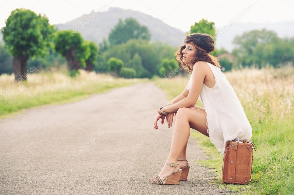 Beautiful girl waiting on a country road with her suitcase
