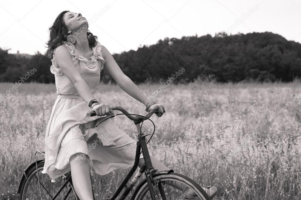 Beautiful black and white image of young woman riding bike in a country road