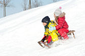 Zwei Kinder rutschen mit Rodeln im Schnee