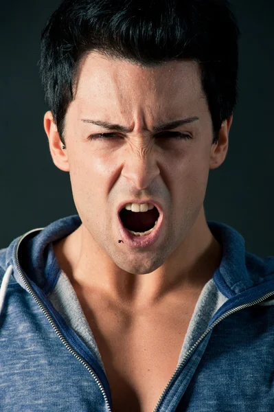 Angry young man shouting on dark background — Stock Photo, Image