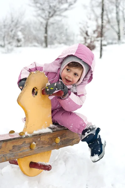 Ung flicka som leker med gungstol i snön — Stockfoto