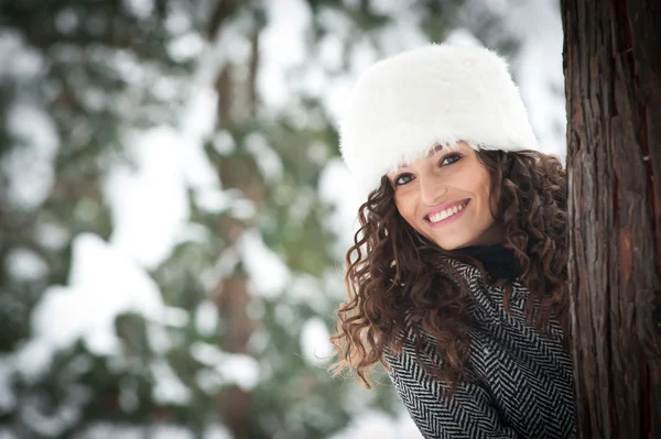 Retrato de menina bonita na neve escondida atrás de uma árvore — Fotografia de Stock