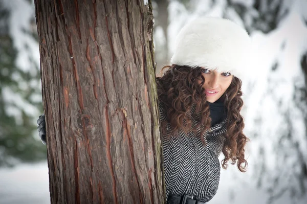 Porträt eines schönen Mädchens im Schnee, das sich hinter einem Baum versteckt — Stockfoto