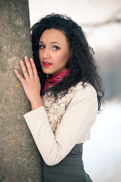 Portrait of beautiful girl in the snow hiding behind a tree — Stock Photo, Image