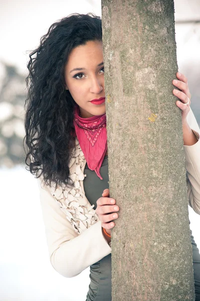 Portrét krásné dívky na sněhu, schovává se za strom — Stock fotografie