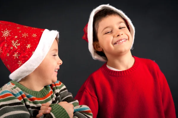 Два брата играют вместе в рождественской шляпе на черном фоне — стоковое фото
