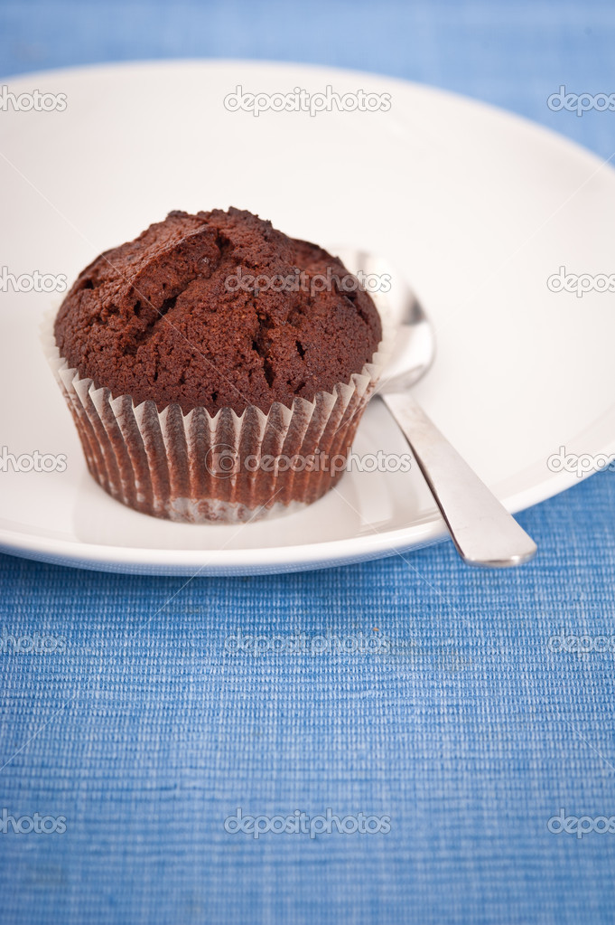 Chocolate muffin on a white plate with teaspoon and blue placemass plate