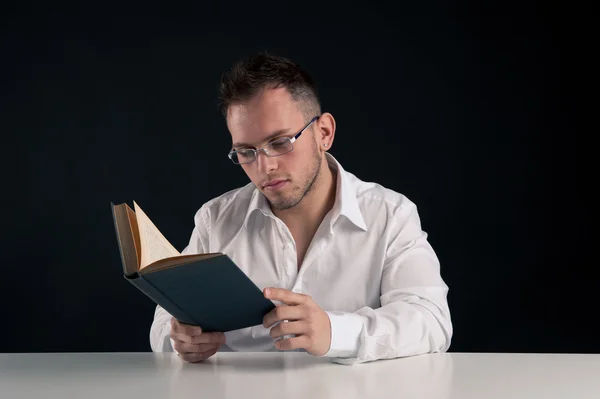 Junger Mann liest ein Buch vor schwarzem Hintergrund — Stockfoto